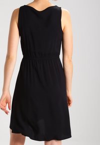Schwarzes ärmelloses Kleid mit einem V-förmigen Rücken, elastischem Bund und leichtem Stoff, der eine glatte Textur und einen knielangen Schnitt aufweist.