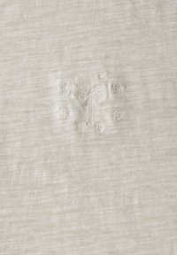 Světle šedá bavlněná látka s jemnou texturou, která obsahuje vyšívané akcenty palmy a text v světle šedé barvě, umístěné centrálně na designu.