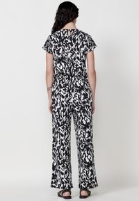 Jumpsuit s černo-bílým vzorem, krátkými rukávy, klíčovou dírou na zádech a širokými nohavicemi; lehký materiál a uvolněný střih.