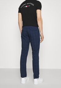 Námořnické kostkované kalhoty se slim fit, s zadními kapsami, spárované s černou košilí s krátkým rukávem s logem. Na nohou bílé tenisky.