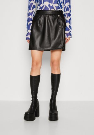 Jupe mini en cuir noir avec une forme légèrement évasée, ornée de trois boutons décoratifs et d'une texture lisse. Assortie à des bottes noires jusqu'aux genoux.