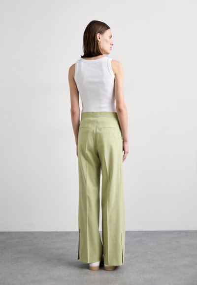 Lichtgroene wijde broek met hoge taille, voorzien van zijsplitten. Gecombineerd met een aansluitend wit tanktop, gezien vanuit de achterkant.