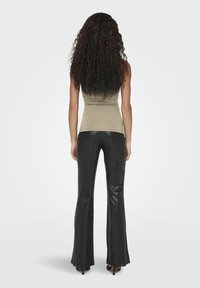 Top aderente color cammello abbinato a pantaloni neri a vita alta e svasati. I pantaloni hanno una texture lucida e l'outfit è completato con scarpe con tacco.