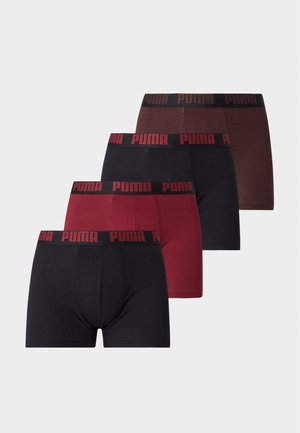 Homme musclé debout pieds nus, bras détendus, portant un boxer Puma marron foncé sur fond blanc uni.