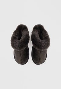 Dark brown slippers with a soft, fluffy gray interior and fold-over collar. They feature a smooth leather exterior and rubber soles.