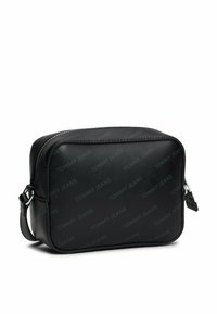 Bolso cruzado sintético negro con forma rectangular, patrón en relieve "TOMMY JEANS", cremallera plateada y correa ajustable.