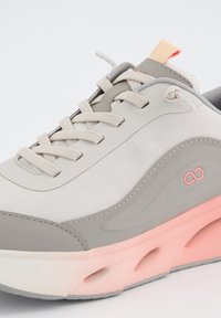 Sneaker grigio chiaro con una tomaia in tessuto testurizzato, dettagli rosa, suola in gomma grigia e un design distintivo a onde. Lacci in tono coordinato.