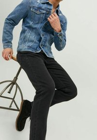 Jeansjacka i ljusblått med slitna detaljer och två bröstfickor, kombinerad med svarta avsmalnande byxor och svarta snörskor.