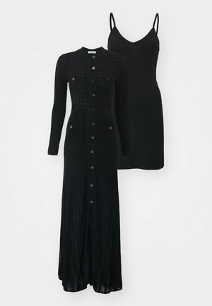 Μαύρο πλεκτό μακρύ καμισό με κούμπωμα και δύο μπροστινές τσέπες, επάνω από ένα μαύρο νυφικό φόρεμα με λεπτές τιράντες.