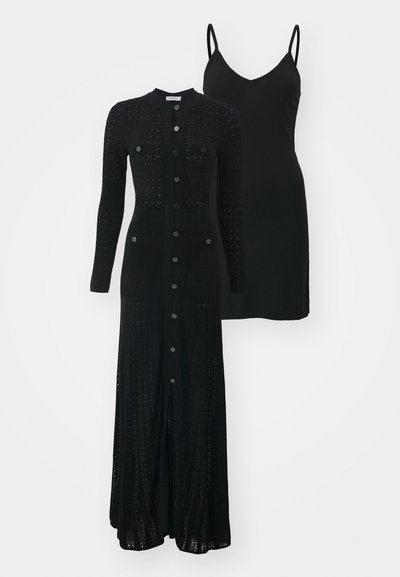 Sort strikket lang cardigan med knaplukning og to frontlommer, lagt over en sort spaghetti strop kjole.