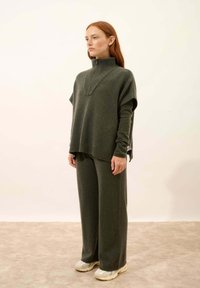 Mörkgrön stickad tröja med hög krage, i kombination med matchande vida byxor. Texturerad tyg, avslappnad passform och subtil detalj med varumärkets tag.