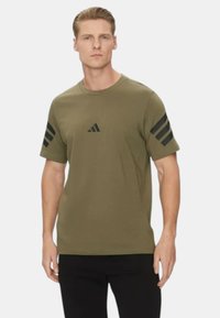 T-shirt in cotone verde oliva con maniche corte, con logo Adidas nero e tre strisce nere su ogni spalla.