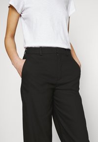 Zwarte op maat gemaakte broek met een soepele textuur, voorzien van een vlakke voorkant, twee zijzakken en een middellange taille. Gemoet met een eenvoudige witte t-shirt.