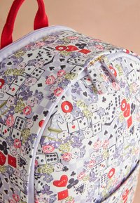 Hátizsák virágos, játékkártya jelképes, dobókockás, sakkbástya és piros szív mintákkal, piros fogantyúval és levendula színű cipzárral, lágy háttérrel.