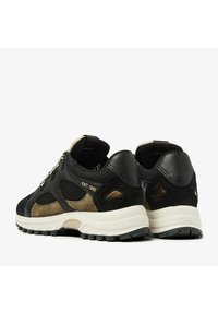 Black and olive green sneakers feature leather and mesh materials, textured accents, a cushioned sole, and "EST. 1992" branding on the heel.