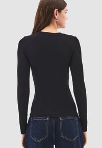 Top nero a maniche lunghe a costine con silhouette aderente, scollatura rotonda e texture liscia, abbinato a jeans di denim blu con cuciture gialle.