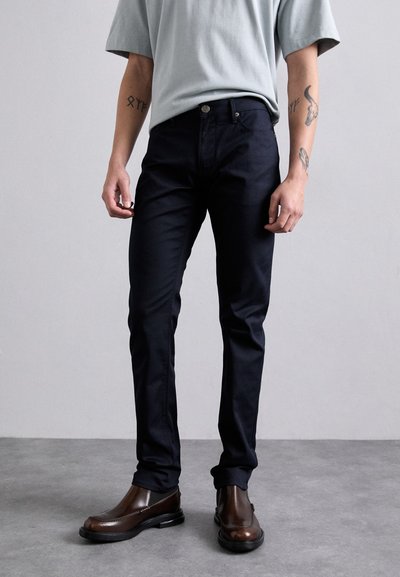 Tengerészkék, slim fit szabású nadrág, pamut keverékből készült, sztenderd derékkal és diszkrét elülső zsebekkel; barna bokapantallal párosítva.