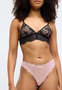 Bralette en dentelle noire avec motif floral et finition, dotée d'un détail de bouton ; associée à un thong en dentelle rose orné d'un accent en nœud.