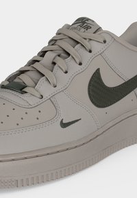 Μπεζ αθλητικό παπούτσι Nike Air Force 1 με λογότυπα Swoosh σε ελαιί πράσινο, μπεζ κορδόνια και λεπτομέρεια με διάτρητο μπροστινό μέρος.