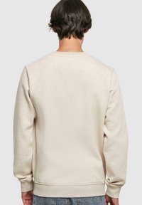 Sudadera beige con mangas largas y puños acanalados, con un cuello redondo y una tela suave y texturizada. Sin marcas ni patrones visibles.