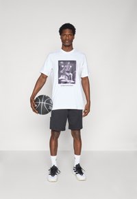 White t-shirt with a black and white basketball graphic, paired with black shorts, holding a basketball, featuring black and white athletic shoes.