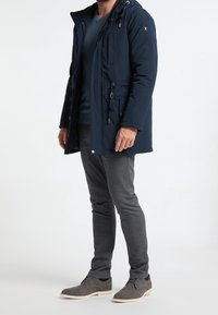 Námořnická parka s kapucí, se zipovým zapínáním, bočními kapsami a stahovacími šňůrkami v pase. Outfit doplňují šedé slim fit kalhoty a šedé boty.