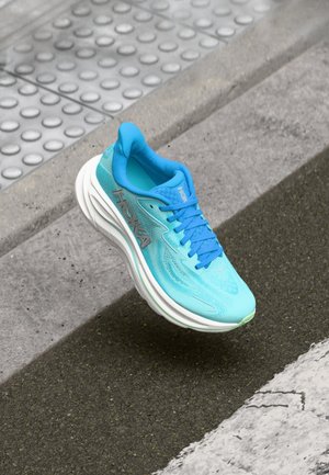 Adidaș albastru cu partea superioară din plasă, închidere cu șireturi și talpă albă cu amortizare. Are un logo pe lateral și modele texturate pe material.