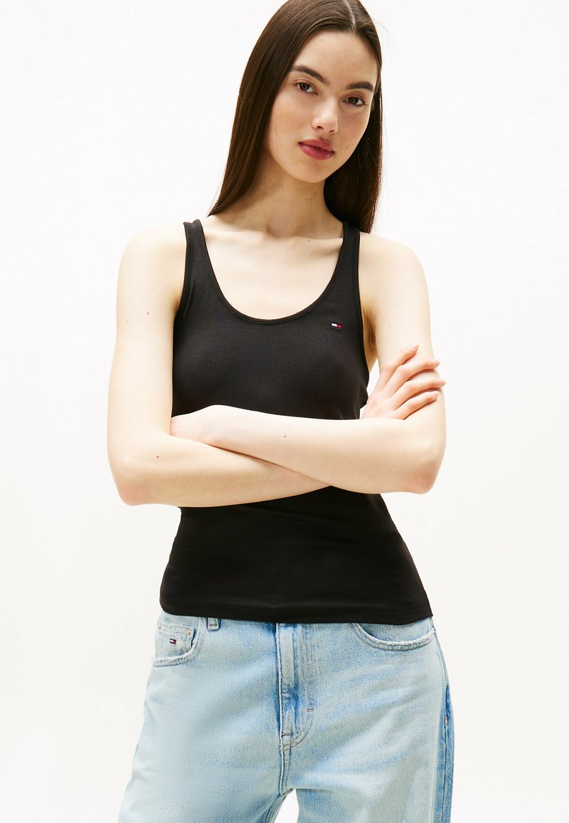 Top de tirantes negro acanalado hecho de algodón, con un escote redondeado y un pequeño logo. Combinado con unos jeans azules claros con una textura sutil.