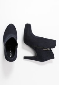 Navy modré semišové kotníkové boty s vysokým podpatkem, bočním zipem, kulatou špičkou a hladkým povrchem.