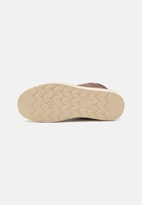 Bruine leren schoen met een gestructureerd oppervlak, voorzien van een crèmekleurige rubberen zool met een zigzagpatroon voor grip en stabiliteit.
