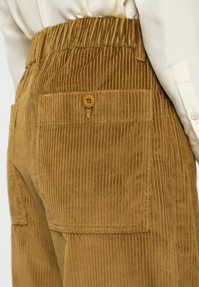 Pantalones de pana marrón con un patrón de relieve texturizado, cinturilla elástica y un bolsillo trasero con detalle de botón.