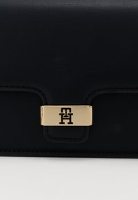 Fekete bőr pénztárca texturált felülettel, aranyszínű csattal, amelyen logó van gravírozva. Elegáns dizájn, igényes varrás részletekkel.