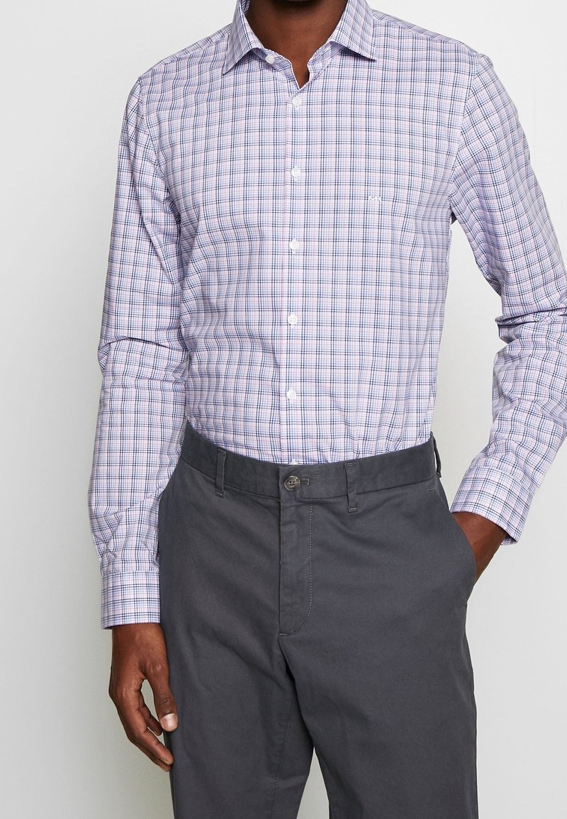 Camicia button-up di un leggero viola con un motivo a quadretti. Presenta maniche lunghe, colletto e una tasca. Abbinata a pantaloni grigi.