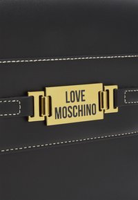 Černá taška z umělé kůže se zlatou obdélníkovou destičkou s nápisem "LOVE MOSCHINO" výrazným černým písmem; kontrastní bílé švy.