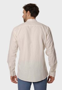Camisa de manga larga color beige claro hecha de lino. Presenta un dobladillo curvado, puños con botón y un diseño de cuello simple.