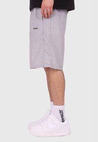 Szare szorty w kratę z bocznymi kieszeniami, elastycznym paskiem w talii oraz naszywką z logo po lewej stronie, zestawione z białymi sneakerami i skarpetkami typu crew.