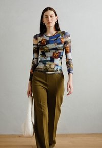 Top a maniche lunghe in tessuto stampato multicolore con immagini a tema viaggio, abbinato a pantaloni a gamba larga verde oliva e una borsa bianca.