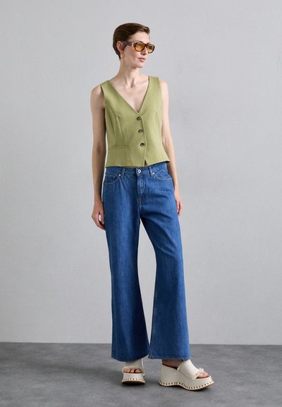 Top verde sin mangas con escote en V y botones, combinado con unos jeans de denim azul de pierna ancha. La modelo lleva sandalias de plataforma de color claro y gafas de sol.