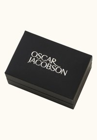 Schwarze rechteckige Box mit glatter Oberfläche. Zeigt das silberne Logo "OSCAR JACOBSON" auf der Oberseite. Die Box hat scharfe Kanten und ein robustes Design.