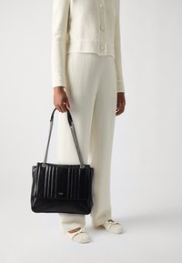 Schwarze Lederhandtasche mit gestepptem Design, Kette und Lederriemen. Verfügt über ein geräumiges Hauptfach und ein Logodetail auf der Vorderseite.