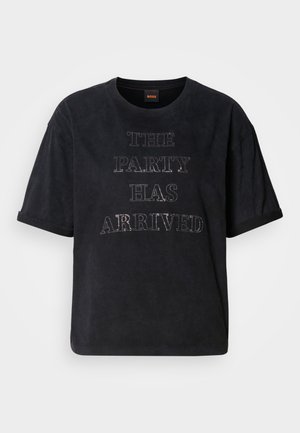 Black t-shirt in soft fabric with a relaxed fit. Features the text "THE PARTY HAS ARRIVED" in silver studs. Crew neckline and short sleeves.