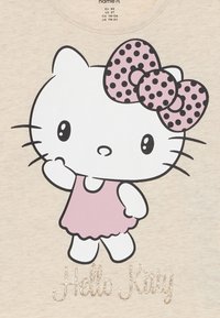 Hello Kitty grafika egy világos bézs színű pólón; rózsaszín ruhát, pöttyös masnit és csillogó szöveget mutat, amely az alján található: "Hello Kitty".