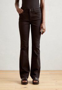 Zwarte flared jeans met een gladde textuur, voorzakken en een knoopsluiting. Gecombineerd met eenvoudige zwarte slide sandalen.