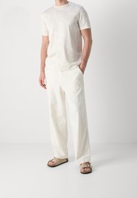 Vit t-shirt med kort ärm och subtilt mönster, matchad med lösa vita byxor och beiga sandaler. Slät textur; avslappnad design.