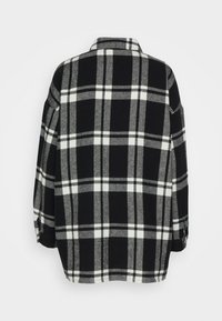 Camicia oversize a quadri bianco e nero con una morbida texture, dotata di colletto, polsini con bottoni e orlo curvo.