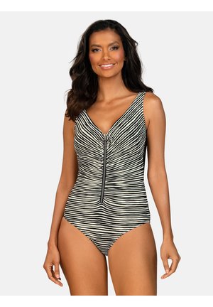 Kobieta uśmiechająca się, ubrana w czarno-biały jednoelementowy strój kąpielowy w paski z przednim suwakiem na jednolitym jasnym tle.