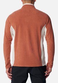 Fleece-Pullover in erdigem Terrakotta mit hellbeigen Seitenpaneelen. Verfügt über einen hohen Kragen, lange Ärmel und eine glatte Textur.
