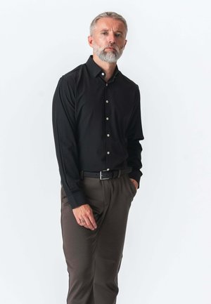 Sort langærmet skjorte med knapper i skræddersyet pasform, båret med brune bukser. Skjorten har en klassisk krave og diskrete knapper.