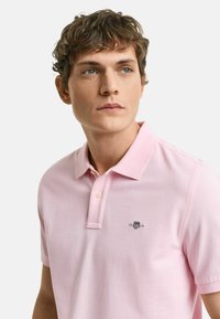 Polo di colore rosa chiaro realizzato in cotone, con un design con colletto, maniche corte e un piccolo logo ricamato sul lato sinistro del petto.