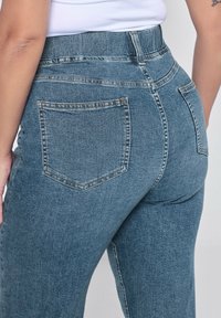 Jean en denim bleu taille haute avec une coupe ajustée, dotés de deux poches arrière et d'une texture légèrement délavée.